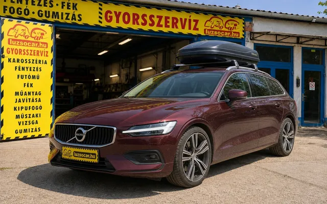 Bordó Volvo kombi tetőboxszal és Luzso Car rendszámtakaróval a műhely előtt